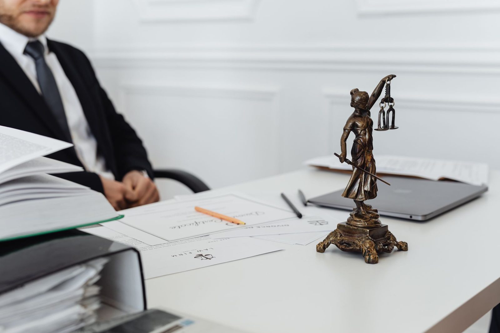 A legal workspace with a Lady Justice statue, case documents, and a laptop on a desk.