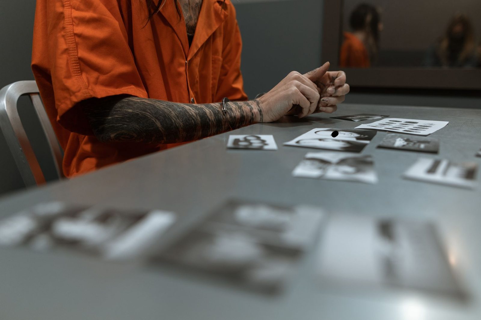 Defendant in orange jumpsuit reviewing case evidence documents in interrogation room.
